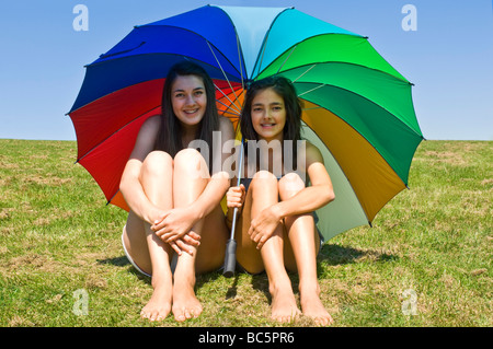 Horizontale Porträt von zwei jungen Schwestern Abschirmung selbst vor Sonne unter einem riesigen bunten Schirm an einem Sommertag Stockfoto