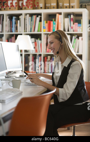 Junge Frau im Büro mit Kopfhörer mit Computer, Porträt Stockfoto