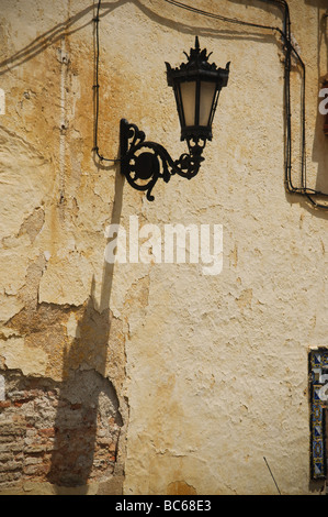 Eine feste Wand Laterne wirft einen dunklen Schatten vor der Sonne auf einer gut getragen Wand in Rhonda, Spanien. Stockfoto