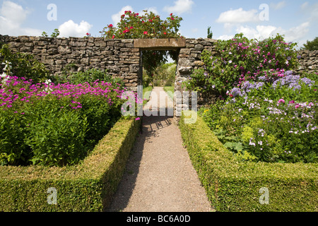 Gartenweg mit niedrigen Kasten Hecke Blumen und Büschen gesäumt und zur Eröffnung in Trockenmauer englischen Landhaus Garten UK Stockfoto