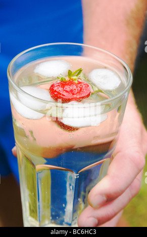 Ein Mann hält einen lange kühlen Drink mit Eis und einer frischen Erdbeere. Birne Cidre. UK Stockfoto