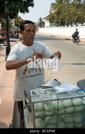 Ein Lao-Mann mit Stäbchen, seine chinesische Knödel aus seiner mobilen Küche in Luang Prabang Laos zu erlegen Stockfoto