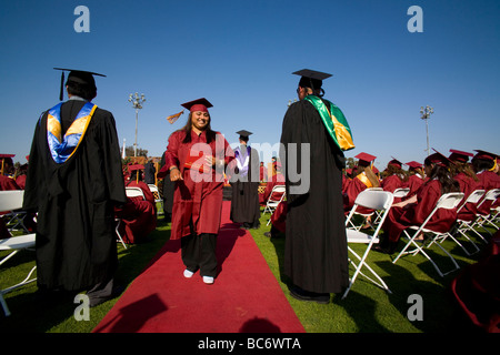 Tragen ihr neues Diplom eine stolze Hispanic Abiturient marschiert zu ihrem Platz während der Abschlussfeier Stockfoto