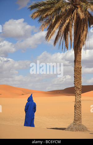 Person trägt traditionelle marokkanische Nonnen unter einer Palme in Erg Chebbi Sanddünen, Sahara Wüste, Merzouga, Marokko Stockfoto