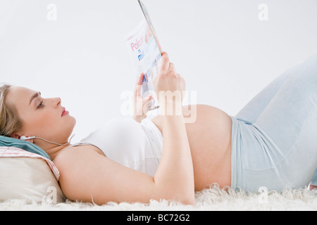 Schwangere Frau liest Magazin und hören Musik Stockfoto
