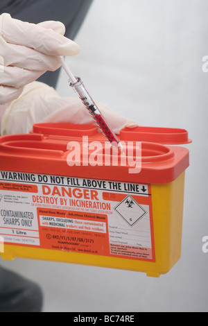 Krankenschwester, Entsorgung von Blut gefüllte Spritze im Krankenhaus "Sharps" Entsorgungsbehälter Stockfoto