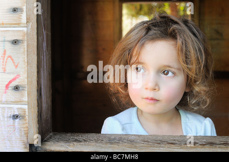 3-jähriges Mädchen mit hellbraune Haare braune Augen blickt Spielhaus Fenster Stockfoto