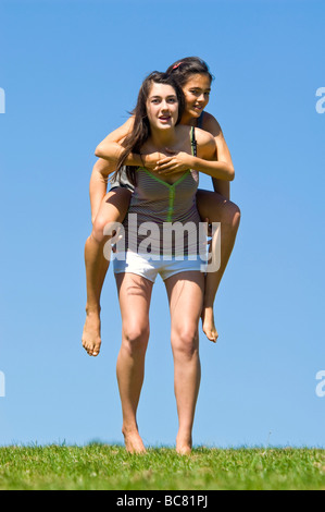 Vertikale Porträt von zwei jungen Schwestern, die mit viel Spaß mit Huckepack reitet auf einem sonnigen Tag Stockfoto