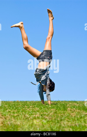 Vertikale Porträt eines attraktiven jungen Teenager Mädchen macht einen Handstand auf dem Rasen an einem sonnigen Tag Stockfoto