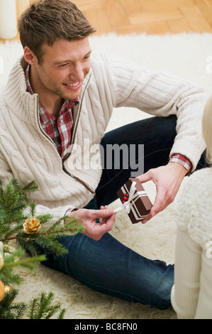 Paar neben Weihnachtsbaum, Mann öffnen Weihnachten Paket- Stockfoto