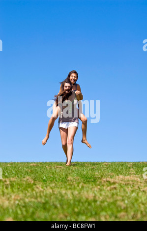 Vertikale Porträt von zwei jungen Schwestern, die mit viel Spaß mit Huckepack reitet auf einem sonnigen Tag Stockfoto