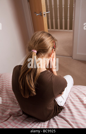 Junges Mädchen sitzt auf ihrem mit dem Rücken zur Kamera, Bettkopf besorgt bei geöffneter Tür. Stockfoto