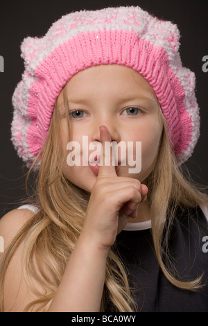 kleines Mädchen, die Finger auf den Mund zu halten, als Stille oder geheimes Zeichen Closeup Portrait auf schwarzem Hintergrund Stockfoto