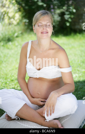 Schwangere Frau mit geschlossenen Augen sitzen auf dem Rasen, Steiermark, Österreich Stockfoto