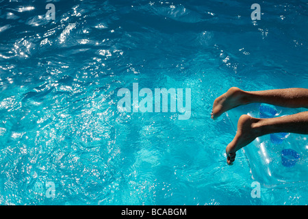 Mans Füße auf einem Lilo in einem blauen Swimmingpool Stockfoto