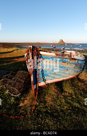 Abend auf Holy Island, ein Fischerboot an der Küste hochgezogen ist Lindisfarne Schloss sichtbar über die Bucht. Stockfoto