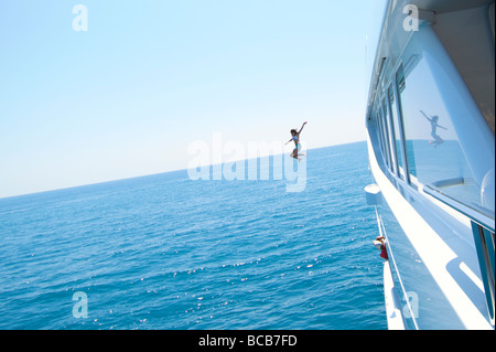 Eine junge Frau springt aus einer großen Luxus-Yacht in das blaue Meer. Stockfoto