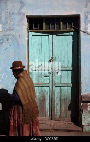 Aymara-Frau in traditioneller Kleidung, vorbei an urigen Tür im Dorf von Guaqui in der Nähe von La Paz, Bolivien Stockfoto
