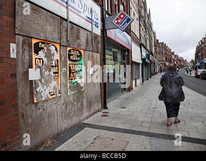 Frau zu Fuß vorbei an Brettern vernagelt Closed Shops in Haupt Straße Barry Wales UK Stockfoto