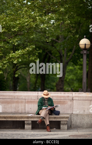 Schwarzer Mann sitzt auf einer steinernen Bank von einem Park und liest die Zeitung in New York USA Mai 2009 Stockfoto