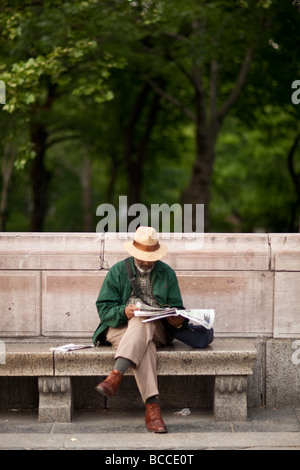 Schwarzer Mann sitzt auf einer steinernen Bank von einem Park und liest die Zeitung in New York USA Mai 2009 Stockfoto