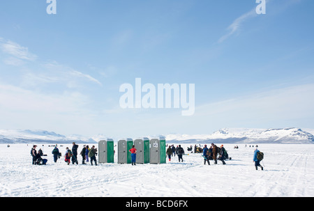 Touristen, die während des Eisanglerwettbewerbs „Vain 2 kalaa“ in Lappland, Finnland, in die Nebengebäude am Lake Kilpisjärvi-Eis Schlange stehen Stockfoto
