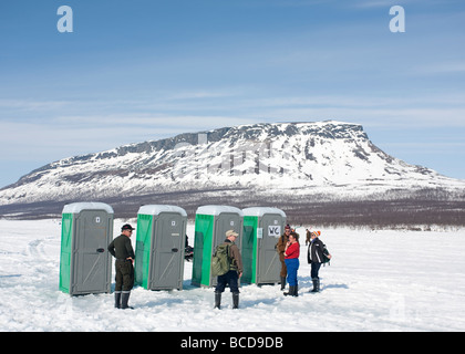 Menschen, die sich während des Eisfischwettbewerbs "Vain 2 kalaa" Saanatunturi Fjell im Hintergrund, Finnland, in mobilen Häusern am See Kilpisjärvi anstellen Stockfoto
