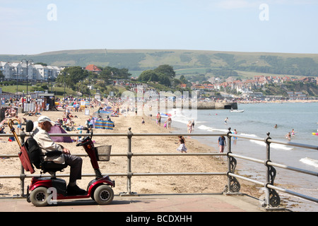 Älterer Mann auf Mobilität Motorroller Blick auf Strand und Meer, Swanage, Dorset, England Stockfoto