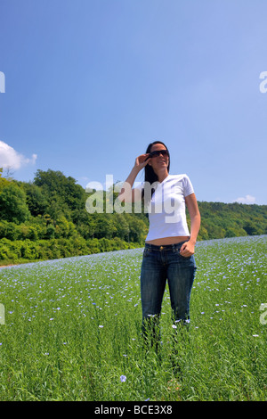 Schöne Brünette Frau in einem Feld von blauen Blüten an einem sonnigen Tag Stockfoto