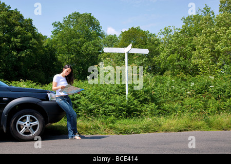 Eine Frau, die an ihr Auto gelehnt, wie sie einer Karte neben ein Straßen Zeichen auf dem Schild steht ist leer für Sie Ihren eigenen Text hinzufügen Stockfoto