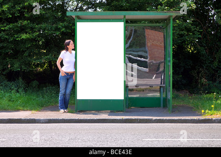 Frau stehend an einer Bushaltestelle mit leeren Plakatwand für Ihre eigene Nachricht Stockfoto