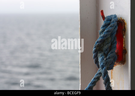 blaues Seil gebunden um eine orange Boot Knagge an der Seite eines Schiffes auf hoher See im Vereinigten Königreich Stockfoto