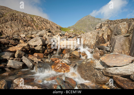 Snowdon im frühen Morgenlicht mit Afon Glaslyn im Vordergrund wie es auf den Bergmann über Felsbrocken in der Nähe von Glaslyn stürzt Stockfoto