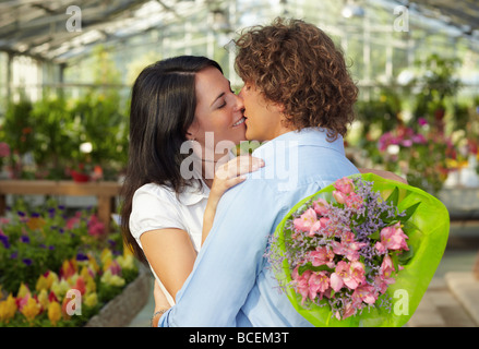 Mitte erwachsenes paar küssen in Blume Kindergarten und holding bouquet Stockfoto