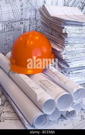 Gelbe, rote Aktenordner, Helm und Haufen von Konstruktionszeichnungen liegen auf dem Tisch. Unternehmen Still-Leben. Stockfoto