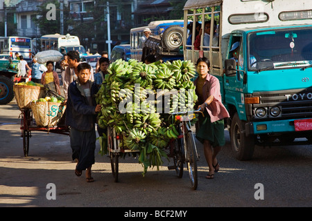 Myanmar, Burma, Yangon. Eine geschäftige Straßenszene in Yangon mit Fahrradrikschas beladen mit Obst in Richtung Markt. Stockfoto