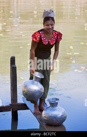 Myanmar, Burma, Mrauk U. Eine junge Frau Rakhine zieht Wasser in den Aluminium-Töpfen aus einem Regenwasser-Teich in der Nähe ihres Dorfes. Stockfoto