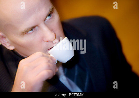 Profil von ein glatzköpfiger Mann in seiner späten 40 trägt einen dunklen Anzug, einen Espressokaffee zu trinken. Stockfoto