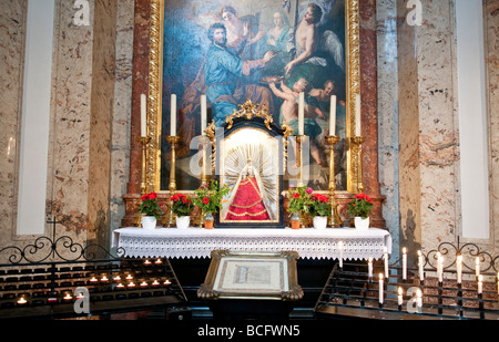 Karlskirche St. Lukas Altar Barockgemälde Madonna Statue Wien Österreich | WIEN, Österreich — Votivkerzen leuchten vor dem St. Lukas Altar in der Karlskirche, sein Hauptgemälde von Daniel Gran zeigt den Evangelisten bei der Arbeit mit Palette und Pinsel. Die Tradition hält Lukas als Schutzpatron der Maler und als Verfasser des ersten Porträts der Jungfrau Maria. In der 1737 geweihten Kirche sind die Leinwände von Gran, Sebastiano Ricci und Martino Altomonte um das Pestgelübde von Kaiser Karl VI. Angebracht. Stockfoto