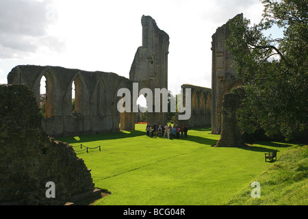 Eine Gruppe von Besuchern bekommen eine Führung von Glastonbury Abbey Ruinen, Somerset, England, UK Stockfoto