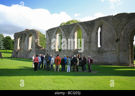 Eine Gruppe von Besuchern bekommen eine Führung von Glastonbury Abbey Ruinen, Somerset, England, UK Stockfoto