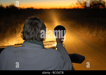 Ranger mit einem Scheinwerfer auf der Suche nach Tieren in der afrikanischen Savanne während einer Nacht Drive, Madikwe Game Reserve, Südafrika Stockfoto