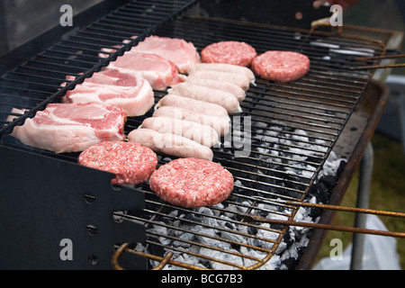 Frisches rohes Fleisch, Burger, Würstchen und Schweinefleisch Koteletts, Kochen auf ein Barbecue-Grill. England, UK. Stockfoto