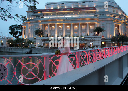 Eine frisch verheiratete Braut posiert auf der Anderson-Brücke vor dem Fullerton Hotel in der Abenddämmerung Stockfoto