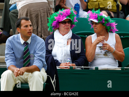 Zwei weibliche Zuschauer tragen lustige Hüte der Wimbledon Farben sitzen in der ersten Reihe bei den Meisterschaften Stockfoto