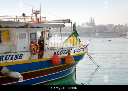 Ein Luzzu (traditionelle maltesische Boot) erwartet die Passagiere für eine Kreuzfahrt rund um den Hafen mit Valletta im Hintergrund, Malta Stockfoto
