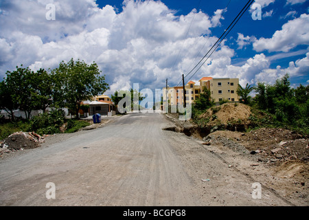 Eine lange gerade Straße mit einem großen ausgegraben Loch an der Seite der Straße führt in eine Stadt in der Nähe von La Torre Dominikanische Republik Stockfoto