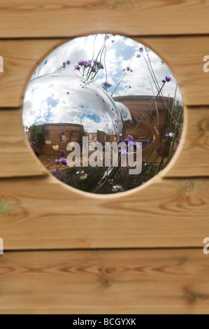 Auf der Suche durch ein Loch im Zaun Panels auf verchromten Kugeln in einer gestalteten Garten. England Stockfoto