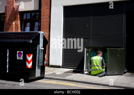 Ein Telefon-Techniker arbeiten auf einer Telefonzentrale in der Straße neben einem großen schwarzen Mülleimer abgebildet. Stockfoto