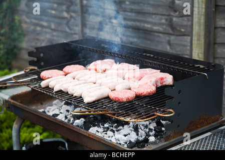 Frisches rohes Fleisch, Burger, Würstchen und Schweinefleisch Koteletts, Kochen auf ein Barbecue-Grill. England, UK. Stockfoto